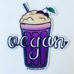 image of a vegan fridge magnet featuring a foamy milk shake in a violet glass. The word "vegan" is displayed over it in a white, curly font