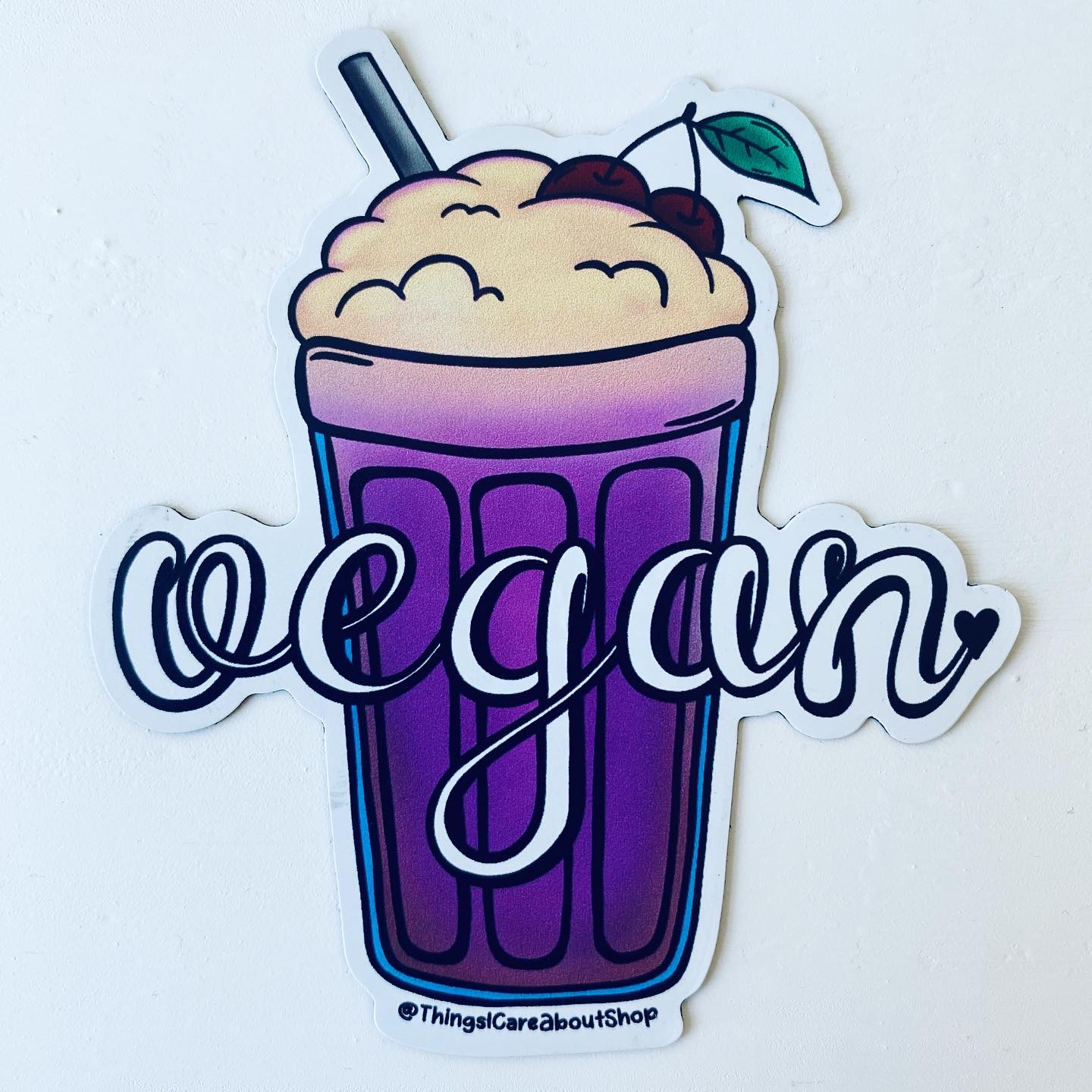 image of a vegan fridge magnet featuring a foamy milk shake in a violet glass. The word "vegan" is displayed over it in a white, curly font