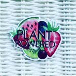 Plant Powered vegan fridge magnet featuring colourful fruits. Die cut shape. Displayed on white basket background