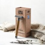 Thin handle light coloured bamboo safety razor next to display box