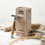 Thick handled light coloured bamboo handled safety razor leaning against display box and storage bag beside
