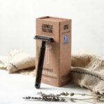 Dark bamboo thin handle safety razor leaning against display box with storage bag beside